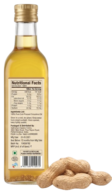 A bottle of peanut cold pressed greenish oil shown from the back, with a gold cap and a label displaying nutritional facts. Several whole peanuts are placed at the bottom right on a white background.