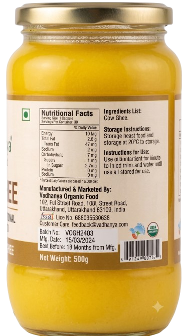 A 500g glass jar of Cow Ghee with a gold metal lid and a white label showing nutritional facts and ingredients. The ghee inside is a rich yellow color.