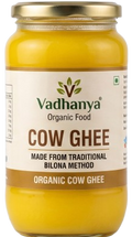 A jar of Vadhanya Organic Food Cow Ghee, showing the yellow ghee inside a clear glass jar with a gold metal lid and a white label.