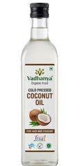 A bottle of Vadhanya Organic Food Cold Pressed Coconut Oil, featuring a clear glass bottle with a black cap and a white label with brown and green accents, set against a plain white background.