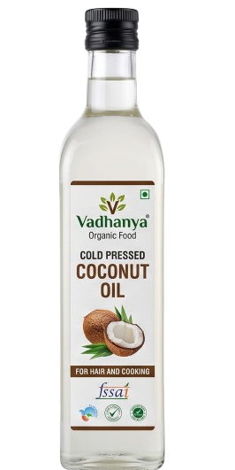 A bottle of Vadhanya Organic Food Cold Pressed Coconut Oil, featuring a clear glass bottle with a black cap and a white label with brown and green accents, set against a plain white background.