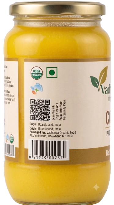 A glass jar of Vadhu Organic Foods Gauravdhari Ghee with a gold metal lid and a white label showing product details, organic certification logos, and a barcode.