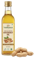 A bottle of Vadhanya Groundnut Oil next to several whole peanuts on a plain white background.