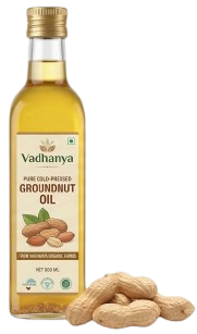 A bottle of Vadhanya Groundnut Oil next to several whole peanuts on a plain white background.
